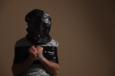 Tied man wrapped in black plastic bag on his head against dark background, space for text. Hostage taking