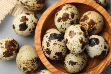 Photo of Wooden bowl and many speckled quail eggs on grey table, flat lay