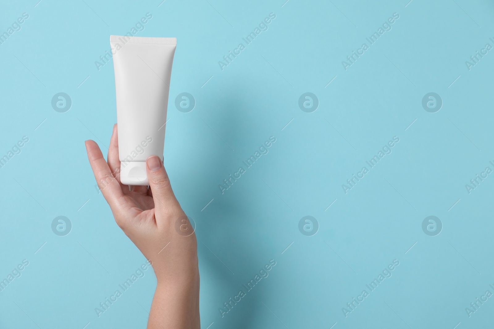 Photo of Woman with tube of hand cream on light blue background, top view. Space for text