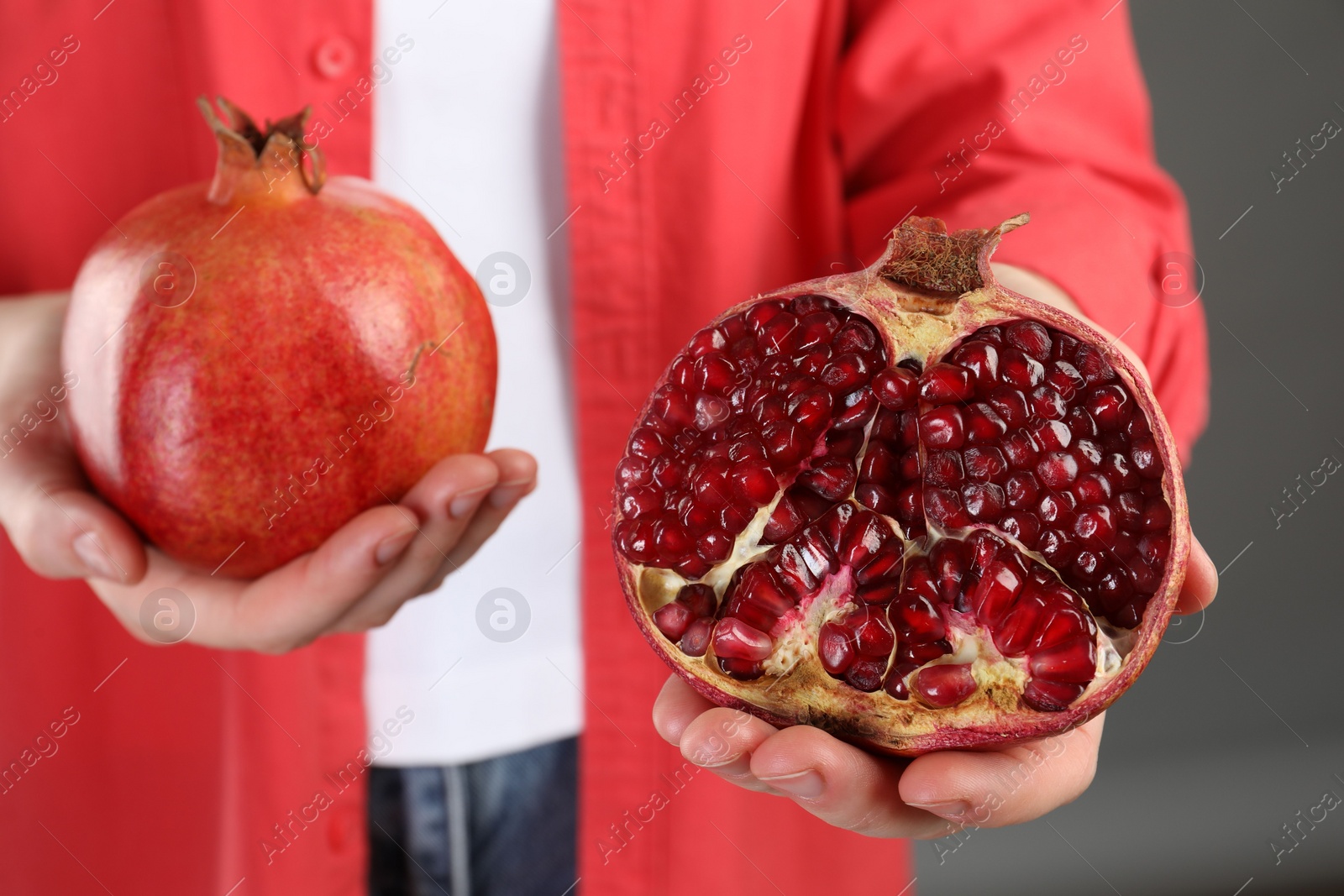 Photo of Woman holding whole and cut pomegranates on grey background, closeup