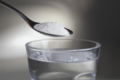 Spoon with baking soda over glass of water on light background, closeup