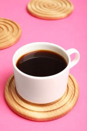 Photo of Cup of coffee and stylish wooden coaster on pink background, closeup