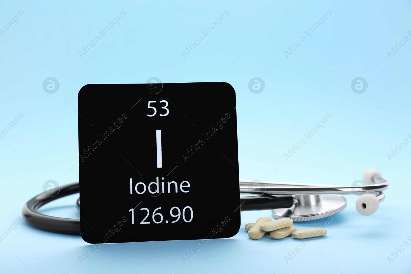 Photo of Card with Iodine element, stethoscope and pills on light blue background