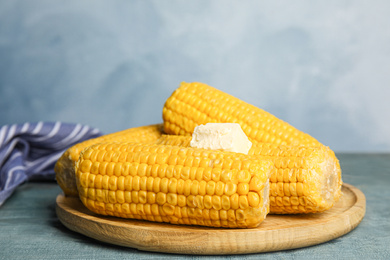 Photo of Delicious boiled corn with butter on light blue wooden table