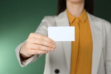 Woman holding white business card on green background, closeup