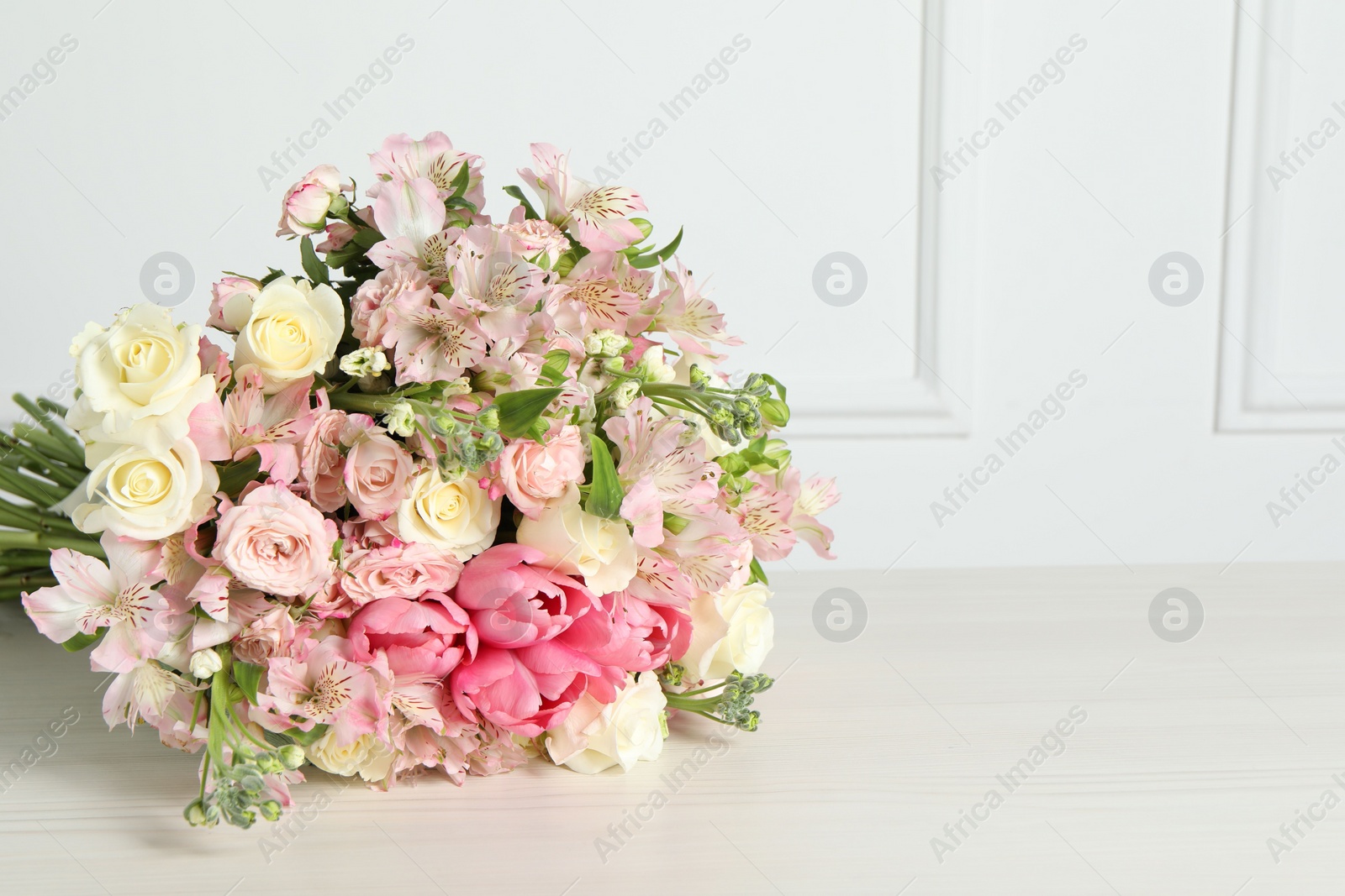 Photo of Beautiful bouquet of fresh flowers on table near white wall. Space for text