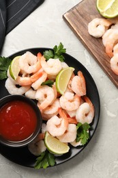 Tasty boiled shrimps with cocktail sauce, parsley and lime on light grey table, flat lay