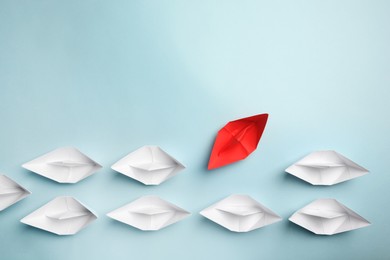 Photo of Red paper boat floating away from others on light background, flat lay with space for text. Uniqueness concept