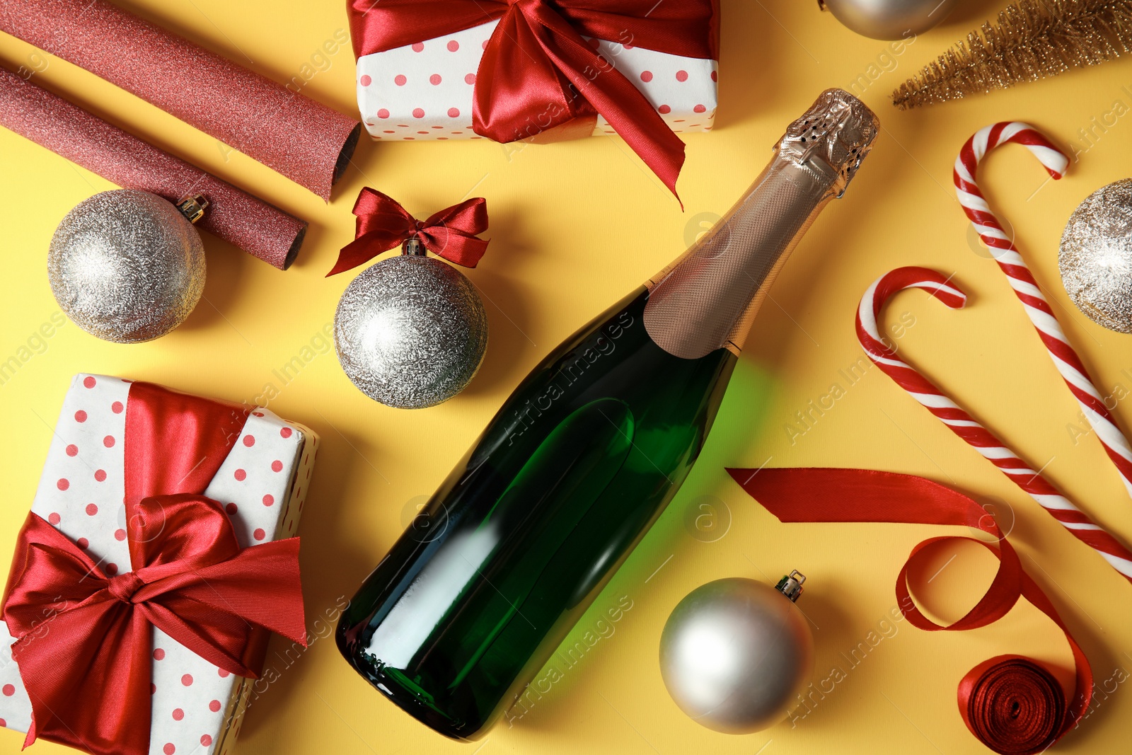 Photo of Christmas composition with bottle of champagne and gifts on color background, top view