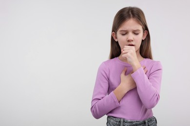 Sick girl coughing on light background, space for text
