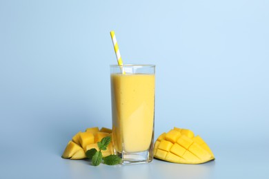 Photo of Glass of tasty smoothie with straw, mango and mint leaves on light blue background