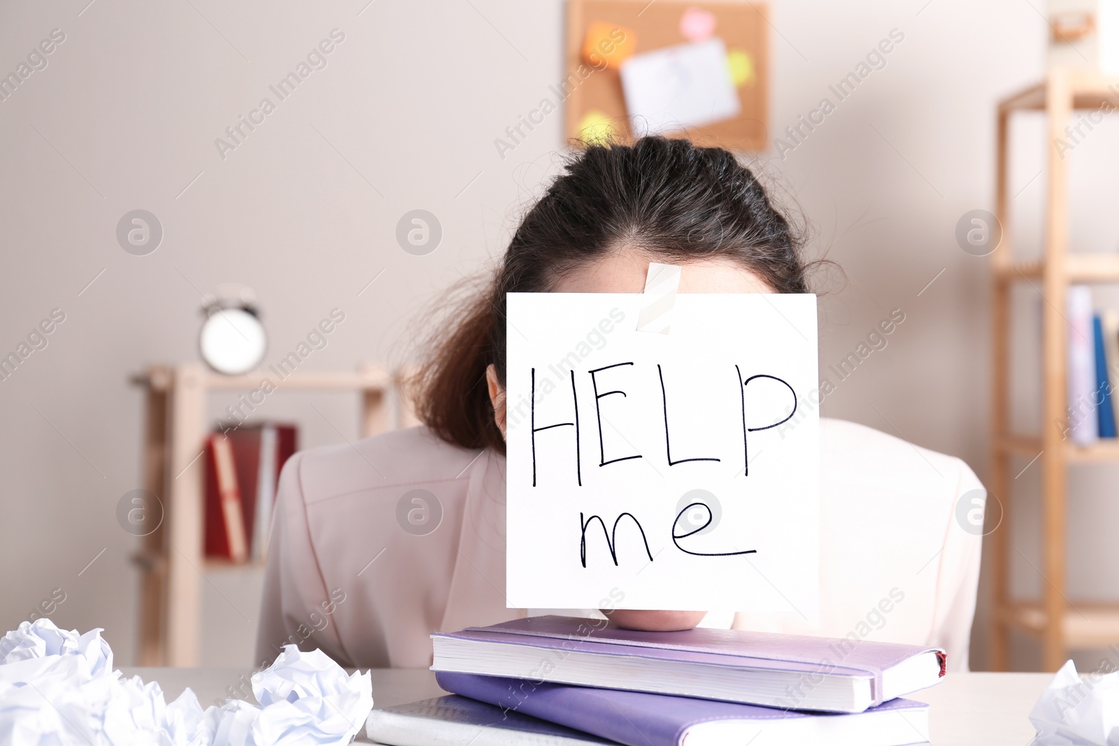 Photo of Young woman with note HELP ME on forehead at workplace