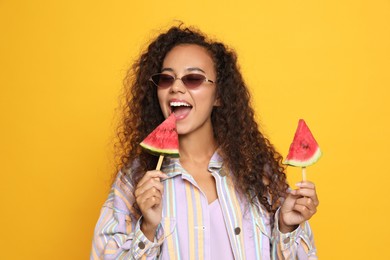 Beautiful young African American woman with pieces of watermelon on yellow background