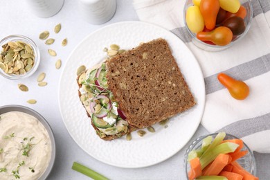 Photo of Tasty vegan sandwich with cucumber, onion, hummus and pumpkin seeds on light grey table, flat lay