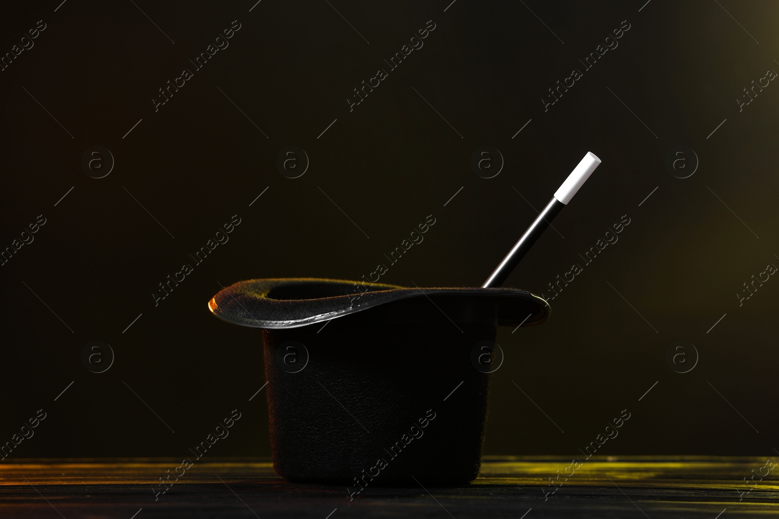 Photo of Magician's hat and wand on wooden table against dark background