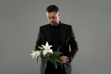 Sad man with white lilies on grey background. Funeral ceremony