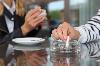 Photo of Woman putting out cigarette in ashtray at table, closeup