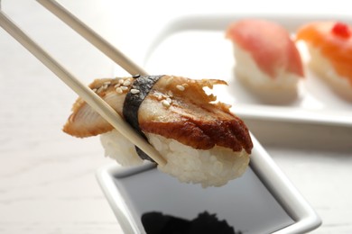 Photo of Dipping delicious nigiri sushi into soy sauce on white wooden table, closeup