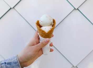 Photo of Woman holding delicious ice cream in waffle cone near white wall, closeup. Space for text