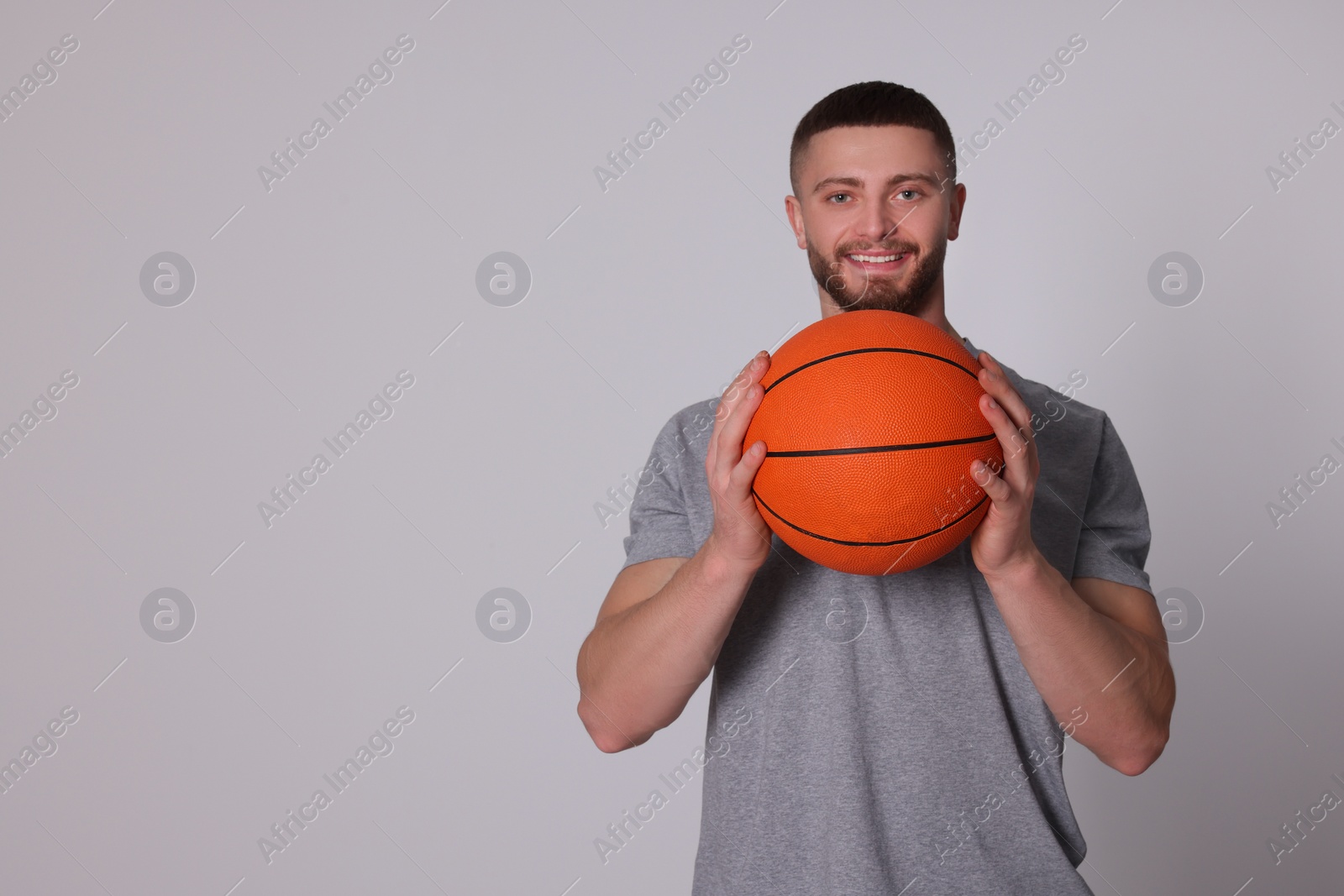 Photo of Athletic young man with basketball ball on light grey background. Space for text