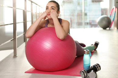 Photo of Lazy young woman with exercise ball on yoga mat indoors