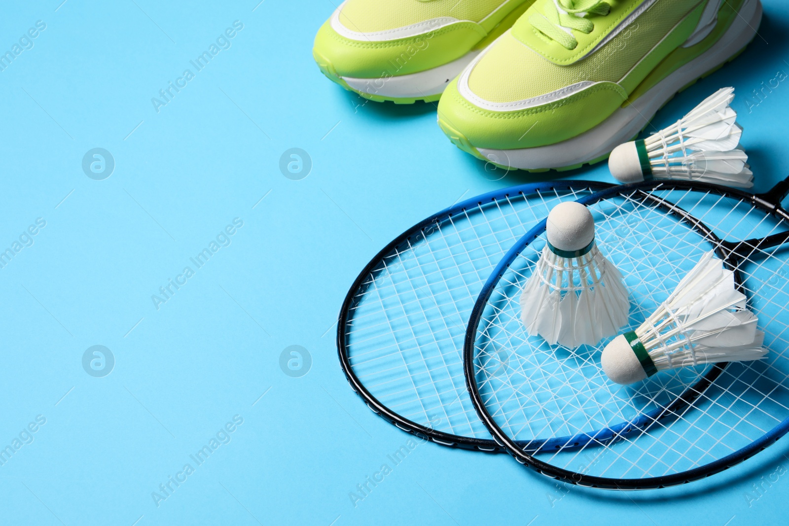 Photo of Feather badminton shuttlecocks, rackets and sneakers on light blue background, space for text