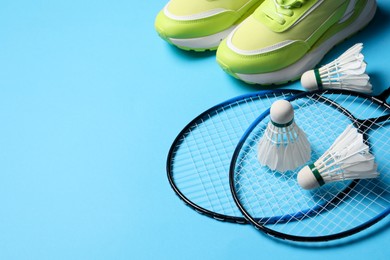 Feather badminton shuttlecocks, rackets and sneakers on light blue background, space for text