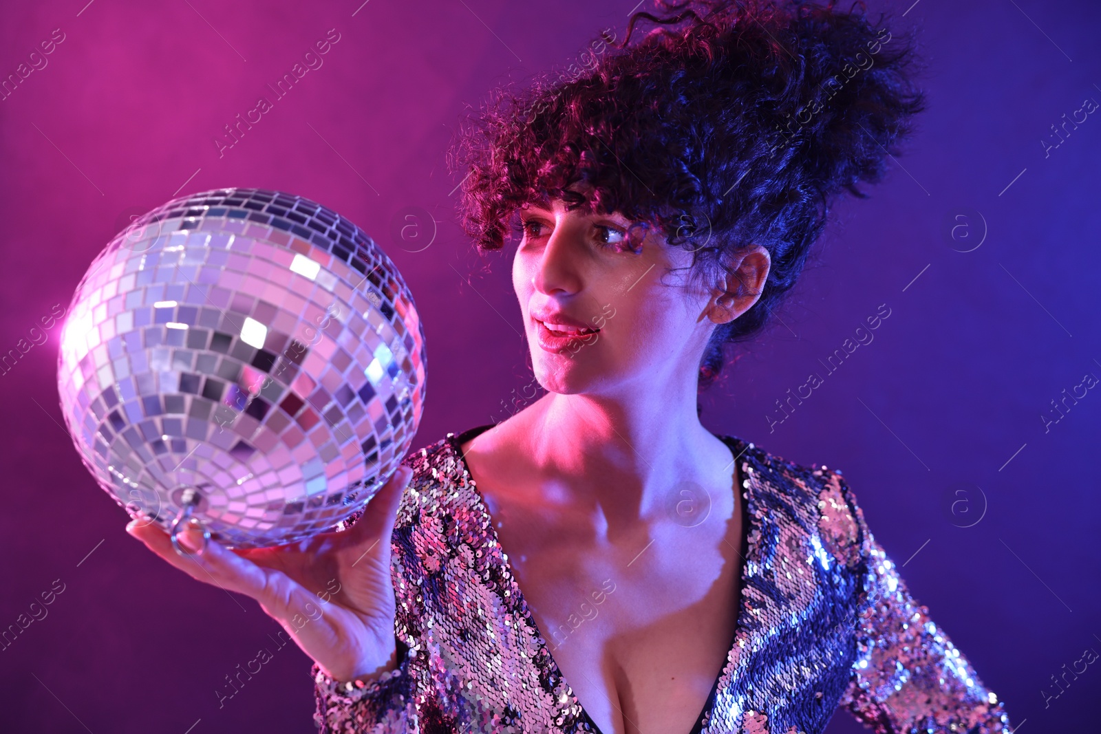 Photo of Beautiful young woman with disco ball posing on color background in neon lights