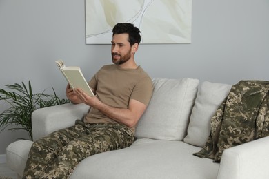 Soldier reading book on soft sofa in living room. Military service