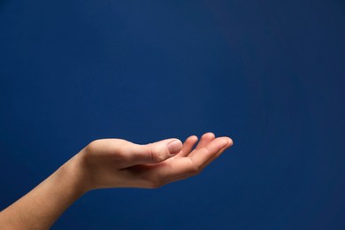 Woman holding something in hand on blue background, closeup. Space for text