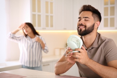 Photo of Man with portable fan enjoying cool air while his girlfriend suffering from heat at home