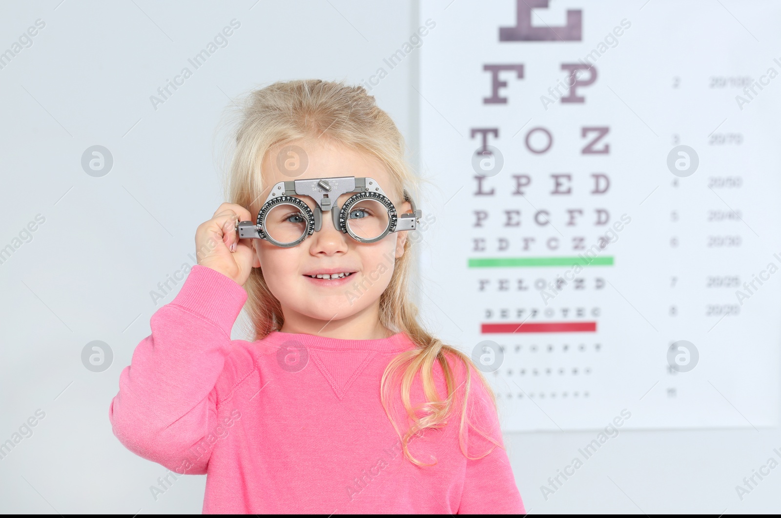 Photo of Little girl with trial frame near eye chart in hospital, space for text. Visiting children's doctor