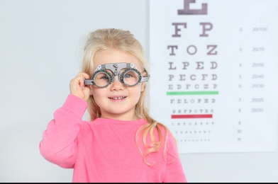 Little girl with trial frame near eye chart in hospital, space for text. Visiting children's doctor