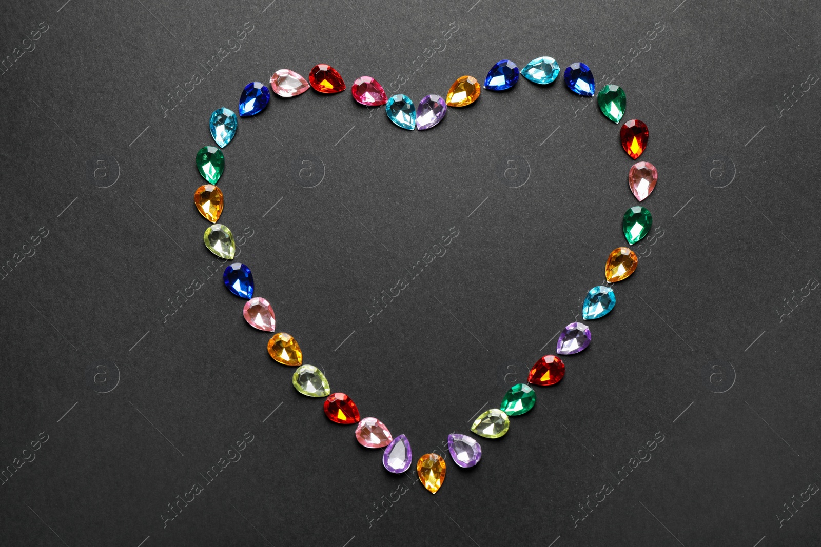 Photo of Heart made of different beautiful gemstones on black background, flat lay. Space for text