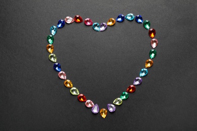 Photo of Heart made of different beautiful gemstones on black background, flat lay. Space for text