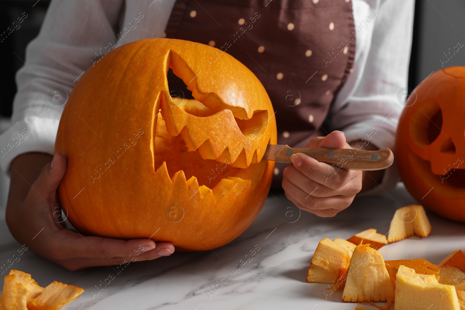 Photo of Woman carving pumpkin for Halloween at white marble table, closeup