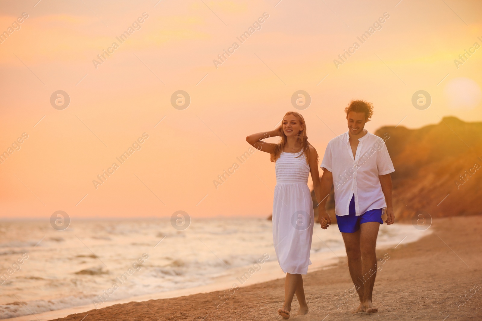 Photo of Young couple walking on beach at sunset