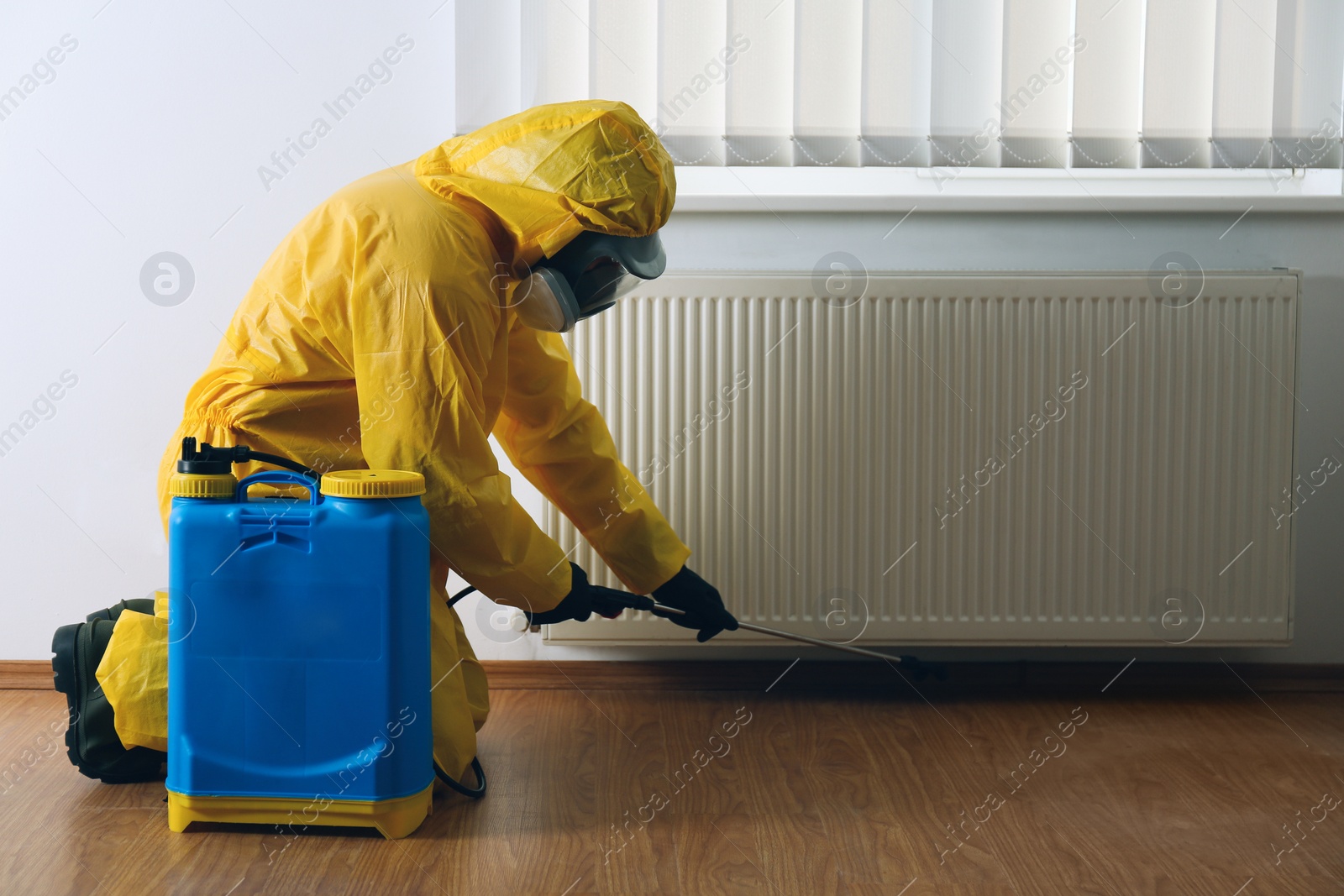 Photo of Pest control worker in protective suit spraying pesticide indoors. Space for text