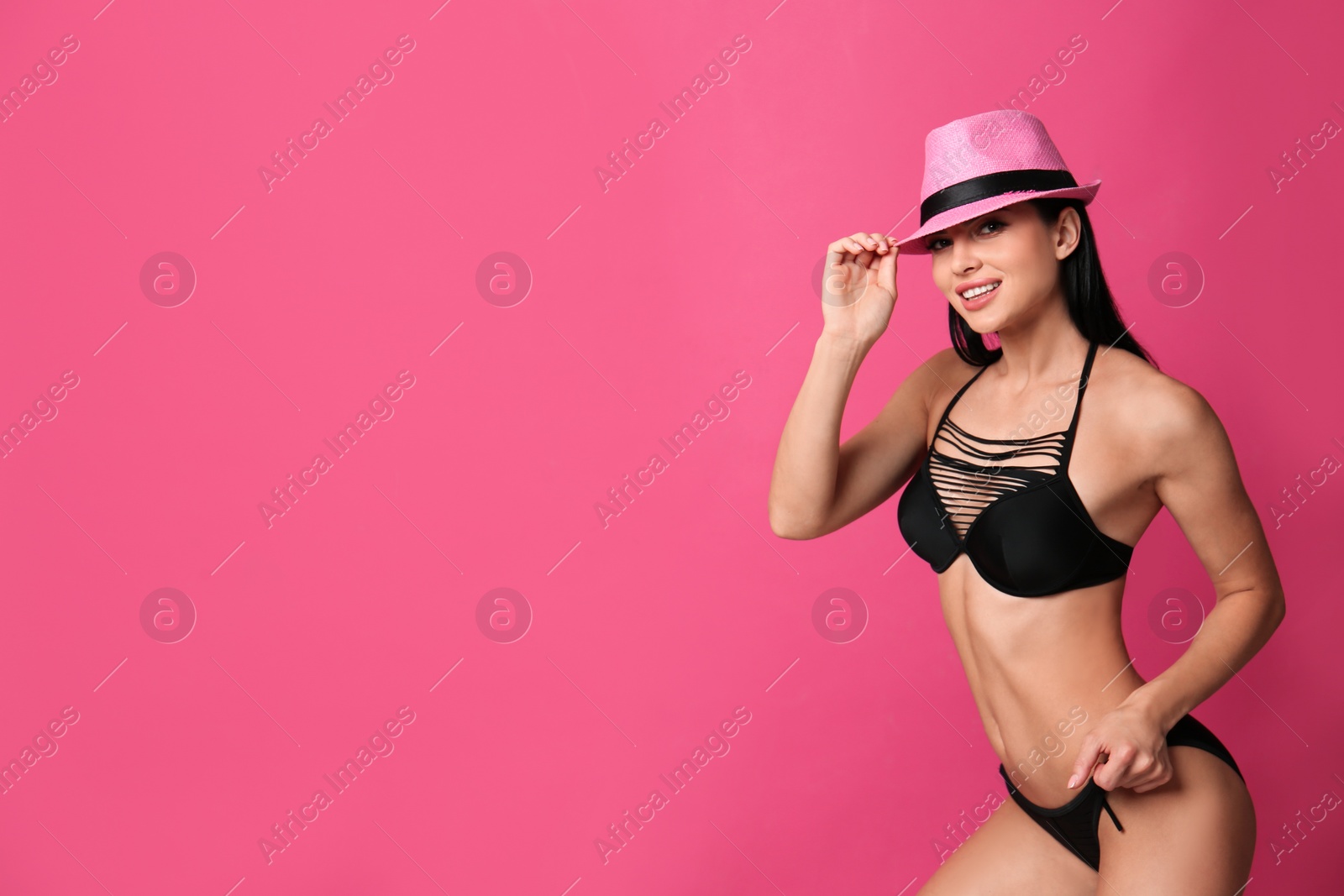 Photo of Beautiful young woman in black bikini with hat on pink background. Space for text