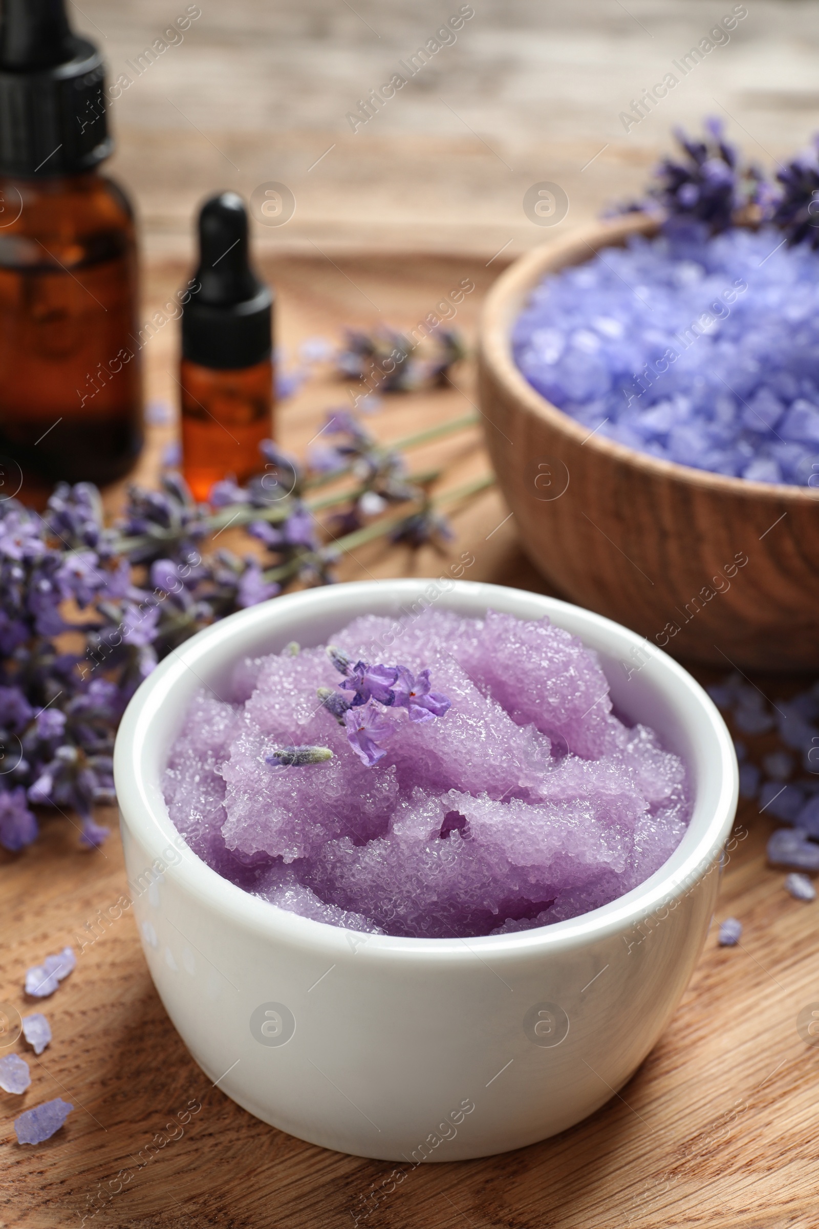 Photo of Bowl of natural sugar scrub and lavender flowers on wooden plate. Cosmetic product