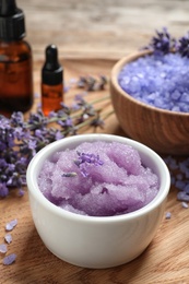 Photo of Bowl of natural sugar scrub and lavender flowers on wooden plate. Cosmetic product