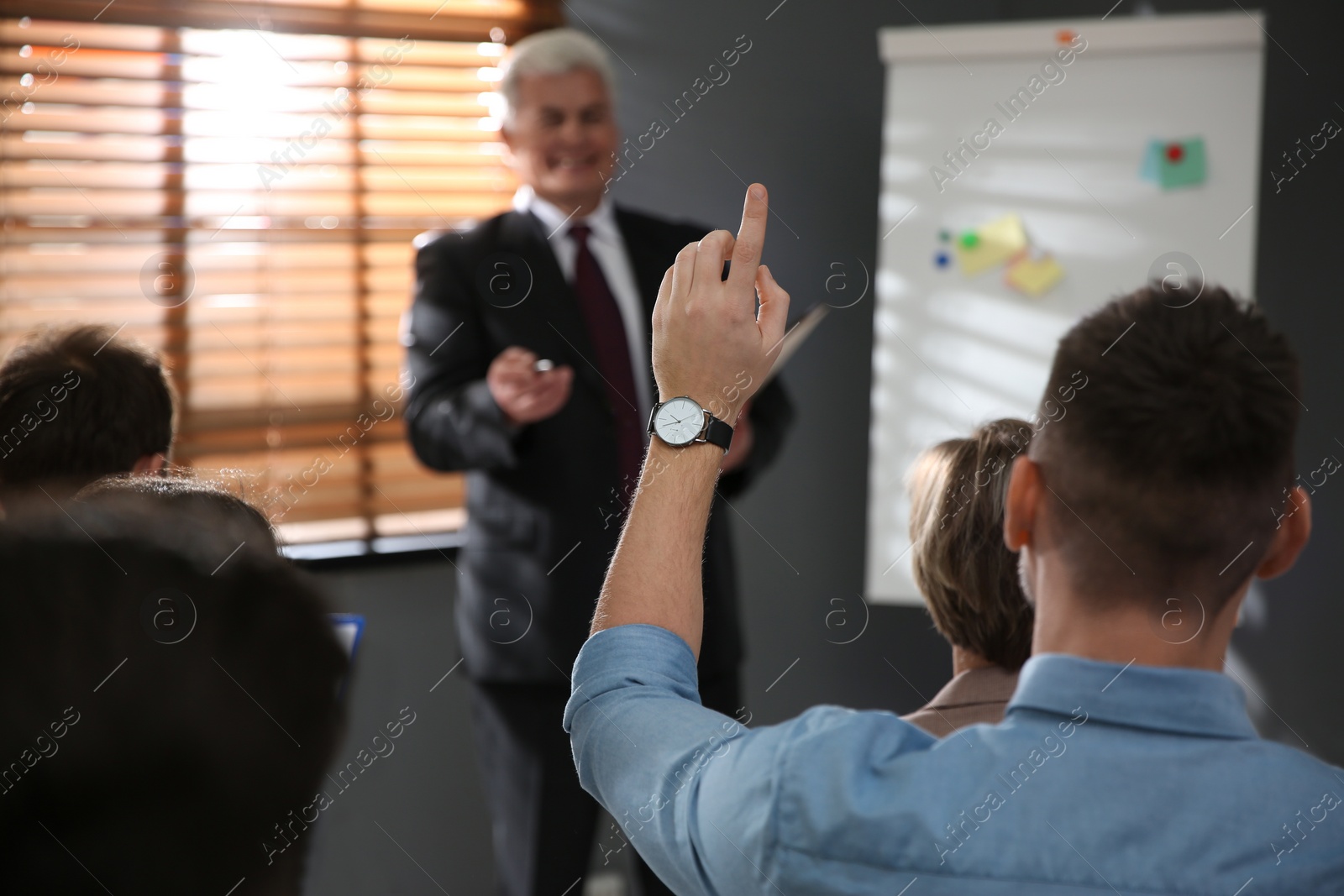 Photo of Man raising hand to ask question at seminar in office