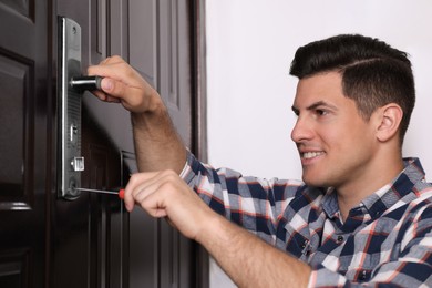 Photo of Handyman with screwdriver repairing door lock indoors