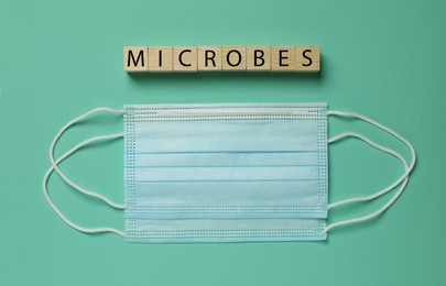 Photo of Word Microbes made with wooden cubes and face masks on turquoise background, flat lay
