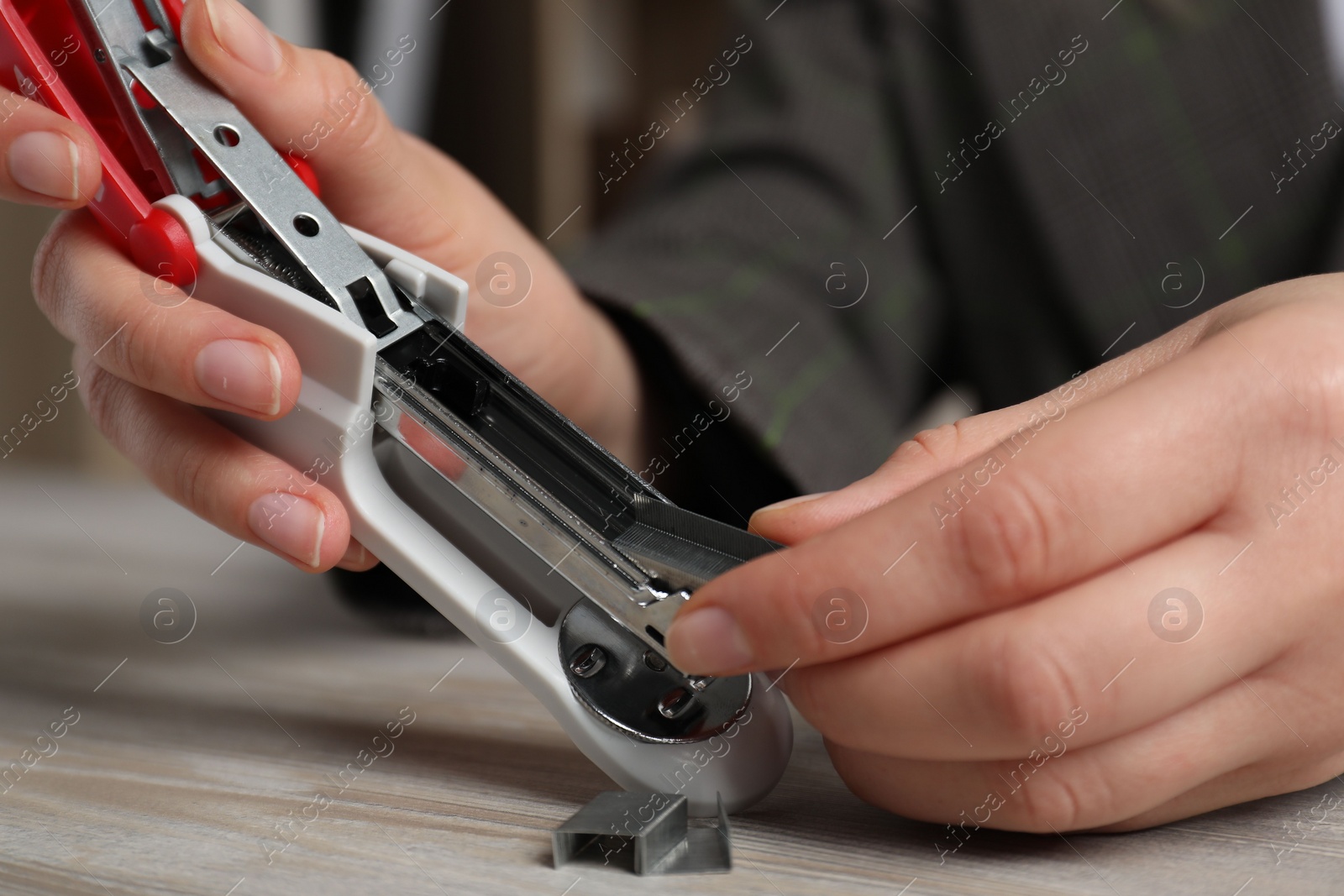 Photo of Woman putting metal staples into stapler at wooden table, closeup