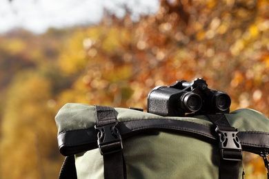 Photo of Backpack with binoculars on blurred background, closeup