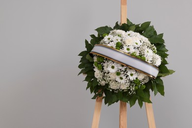 Photo of Funeral wreath of flowers with ribbon on wooden stand against grey background. Space for text