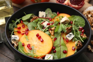 Tasty salad with persimmon, blue cheese, pomegranate and walnuts served on wooden table, closeup