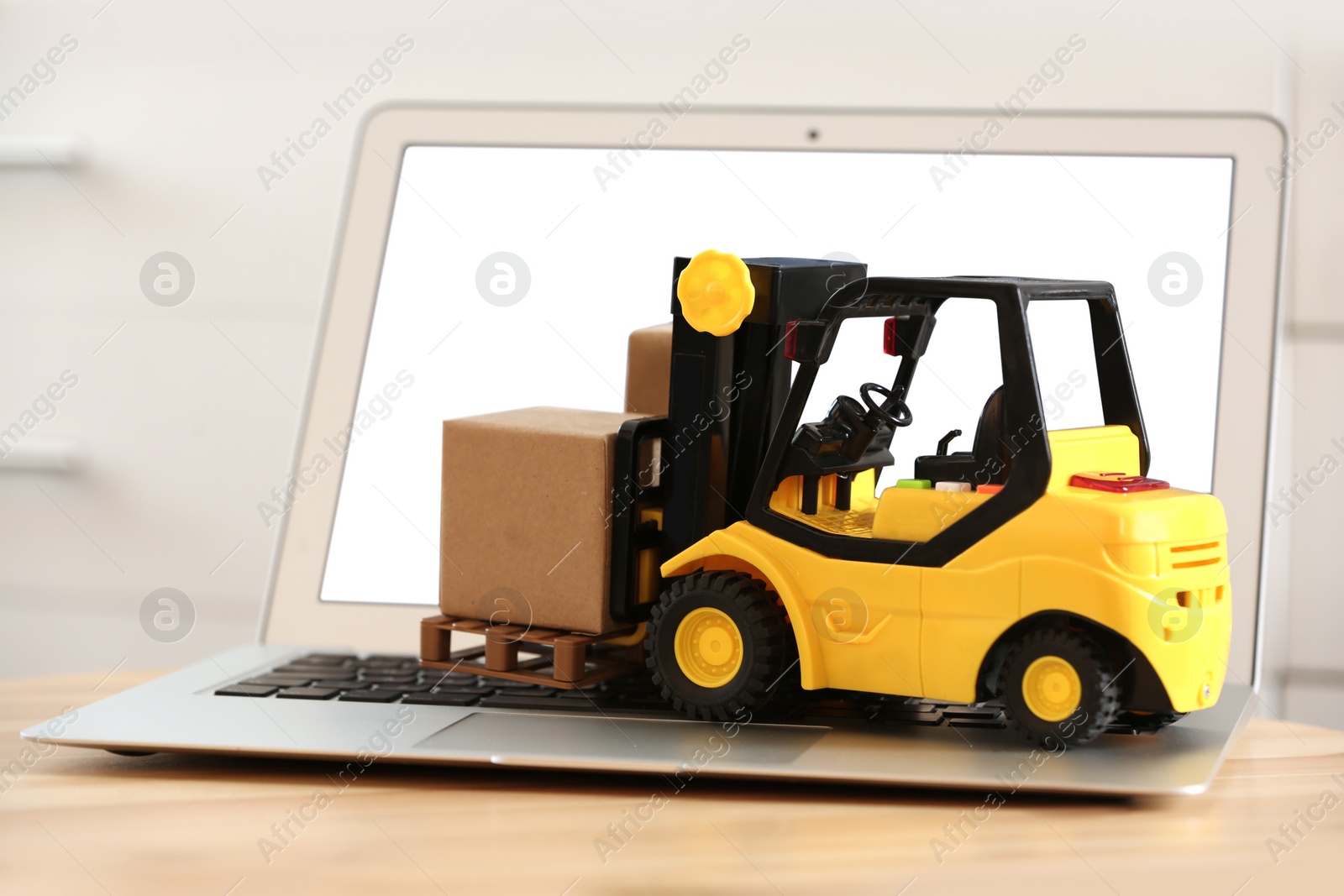 Photo of Laptop and forklift model with boxes on table indoors. Courier service