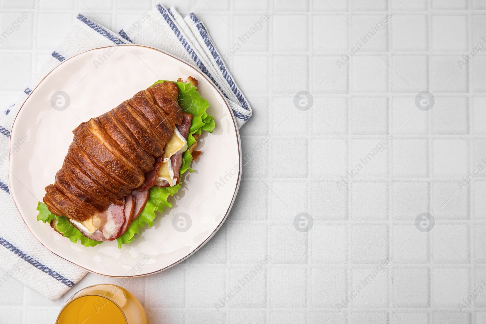 Photo of Tasty croissant with brie cheese, ham and bacon on white tiled table, flat lay. Space for text